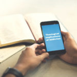 Man holding smartphone that displays the title text of this Crosspoint podcast episode: Theological Implications of Addiction.